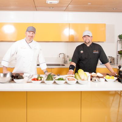 two chefs standing in a kitchen with food on display
