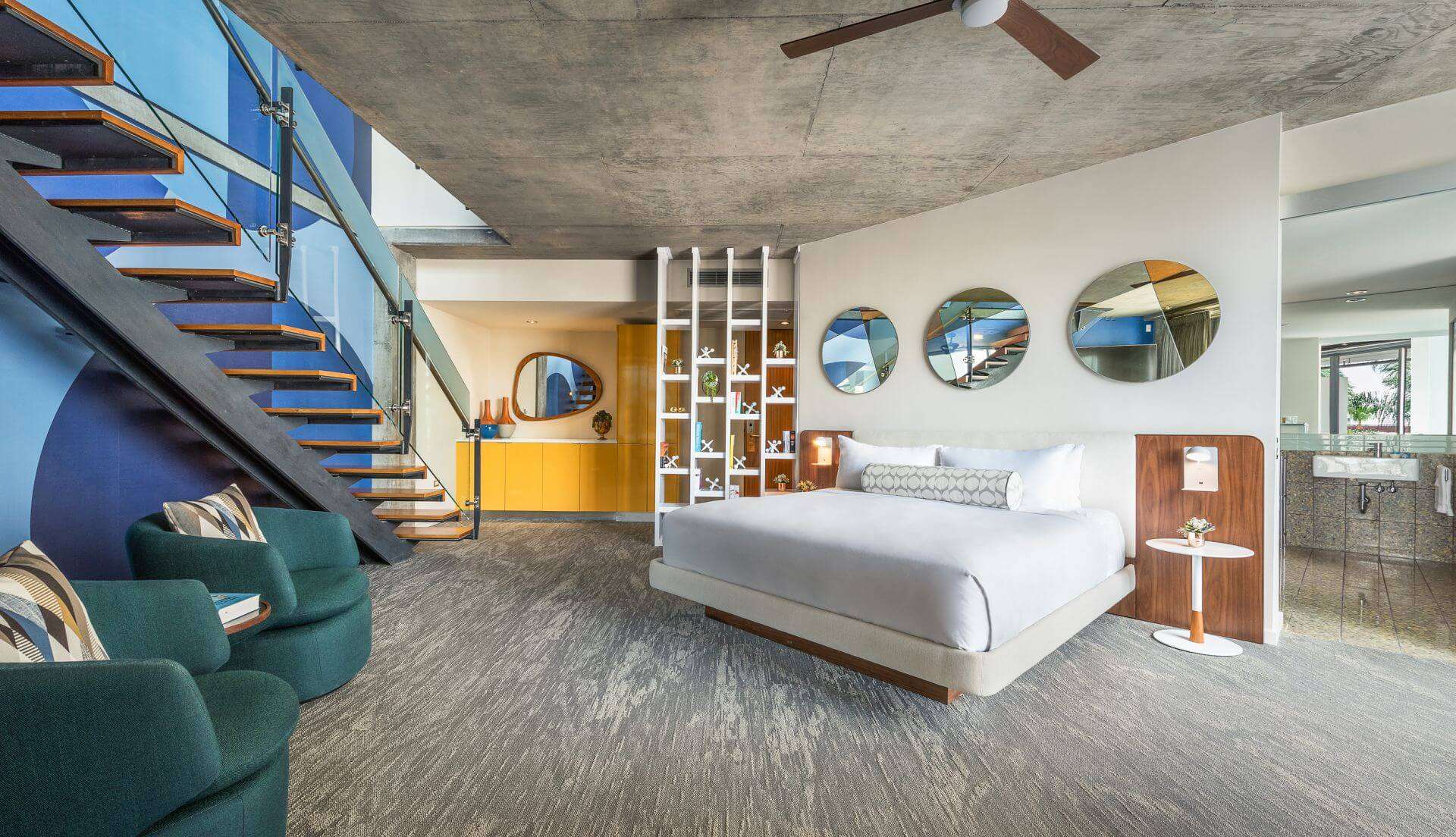 The Loft Suite bedroom featuring a large bed beside a set of stairs and two chairs.
