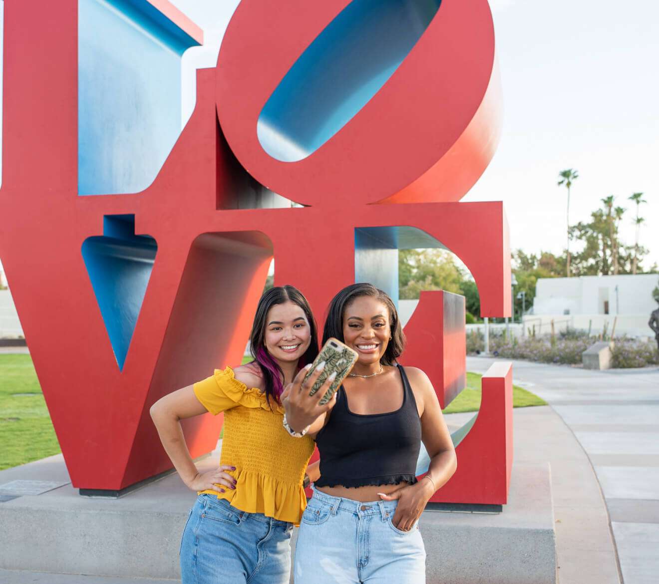 Friends pose joyfully near a love sculpture.
