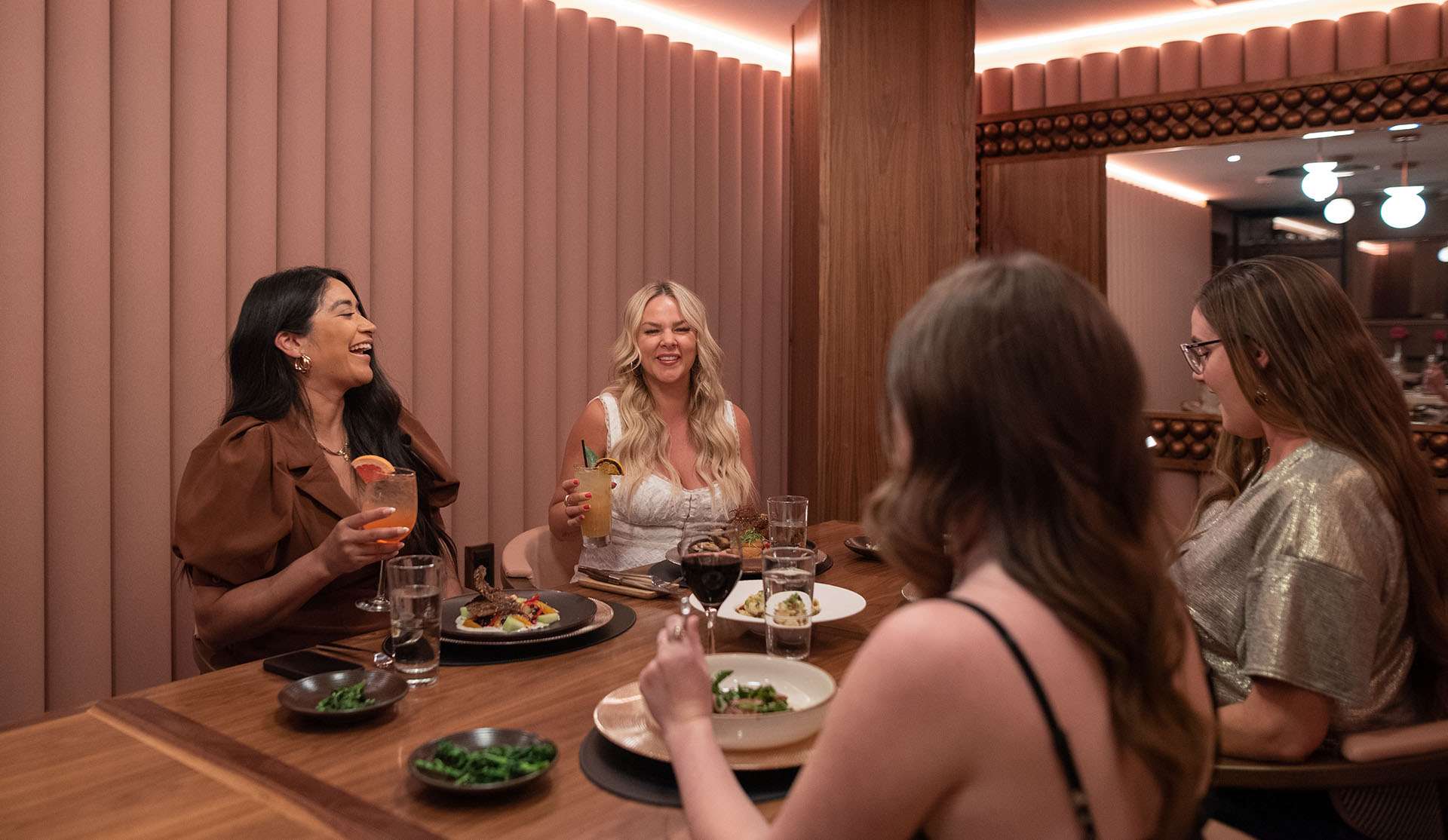 4 Women sitting at a table with food and drinks in front of them.