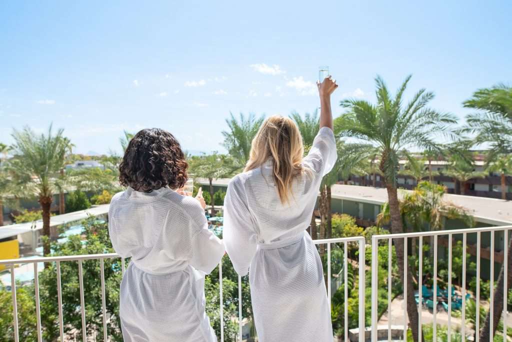 two women in spa robes on the balcony facing the view with sparkling wine