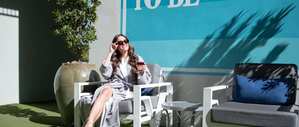 woman sitting in chair in front of spa mural with a cocktail in hand