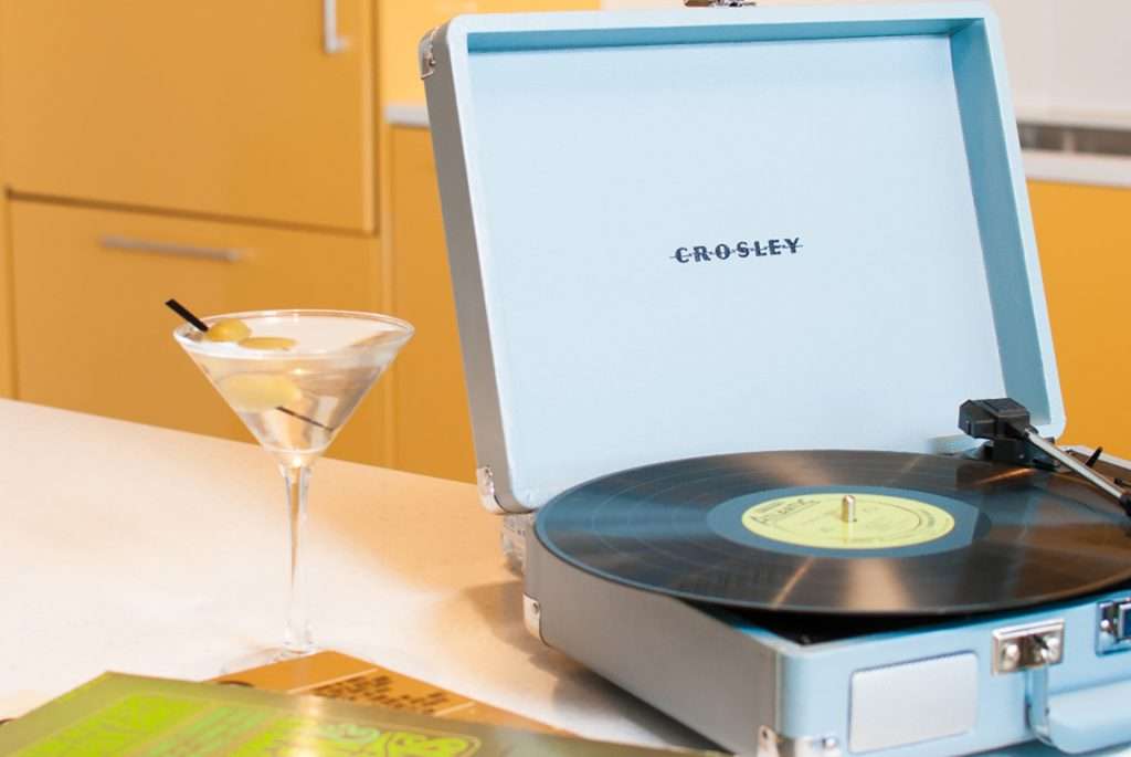 A record player with a martini and stack of magazines beside it.