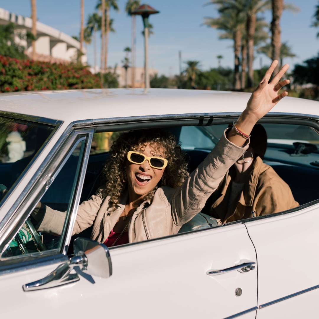 woman driving a vintage car smiling with her arm out the window